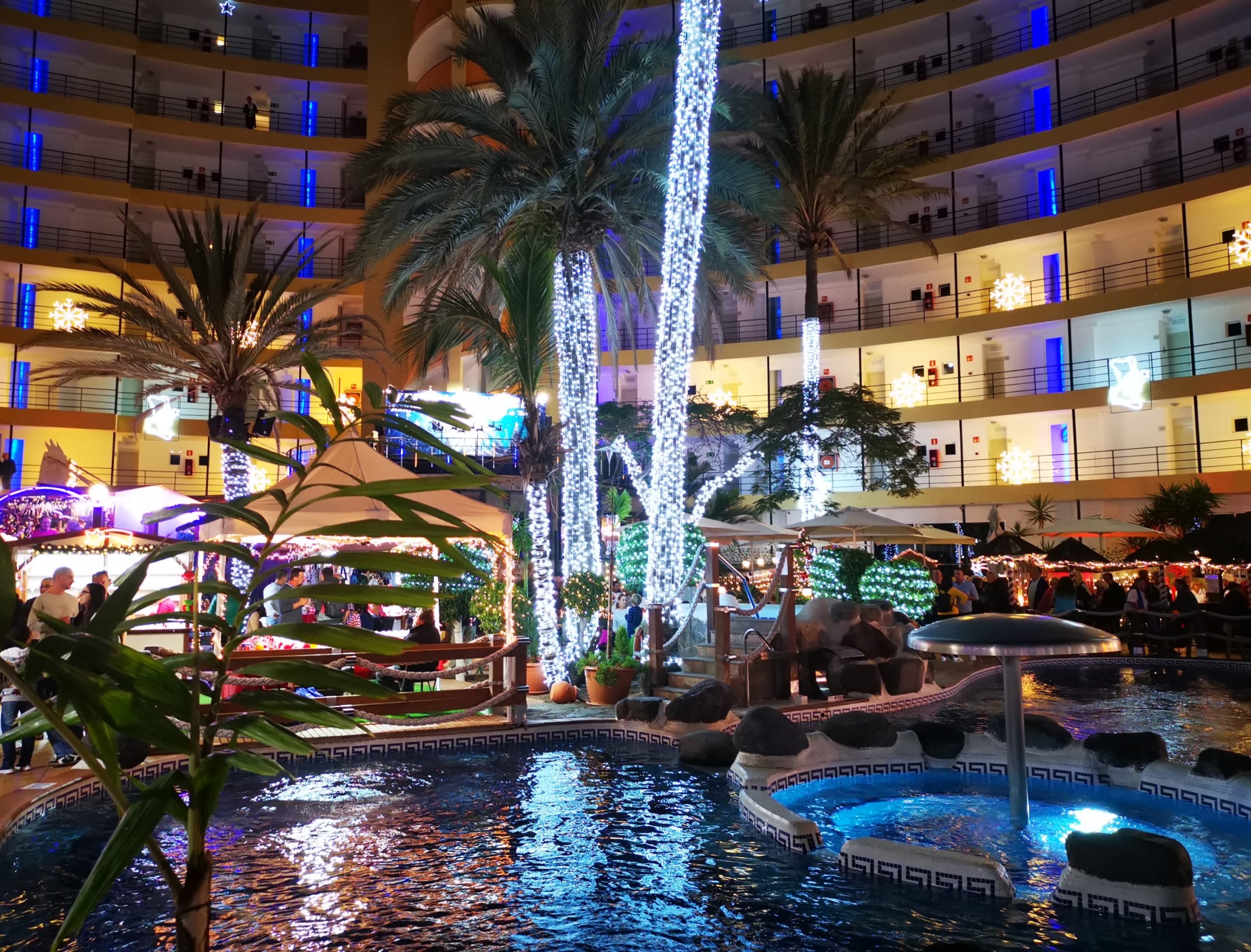 Blick vom Pool auf den Weihnachtsmarkt, im Hintergrund Palmen  mit Licht dekoriert